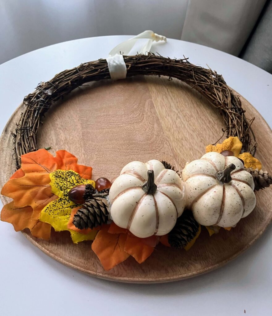 Dekoracja jesienna w formie wianka, łącząca naturalną bazę z elementami kojarzącymi się z jesienią: dynie, szyszki, kasztany i barwne liście.