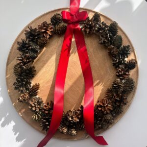 Ręcznie robiony wieniec świąteczny z naturalnych szyszek na drewnianej bazie, ozdobiony czerwoną satynową wstążką i kokardą. Rustykalna, bożonarodzeniowa dekoracja w stylu skandynawskim, idealna na drzwi, ścianę lub nad kominek.