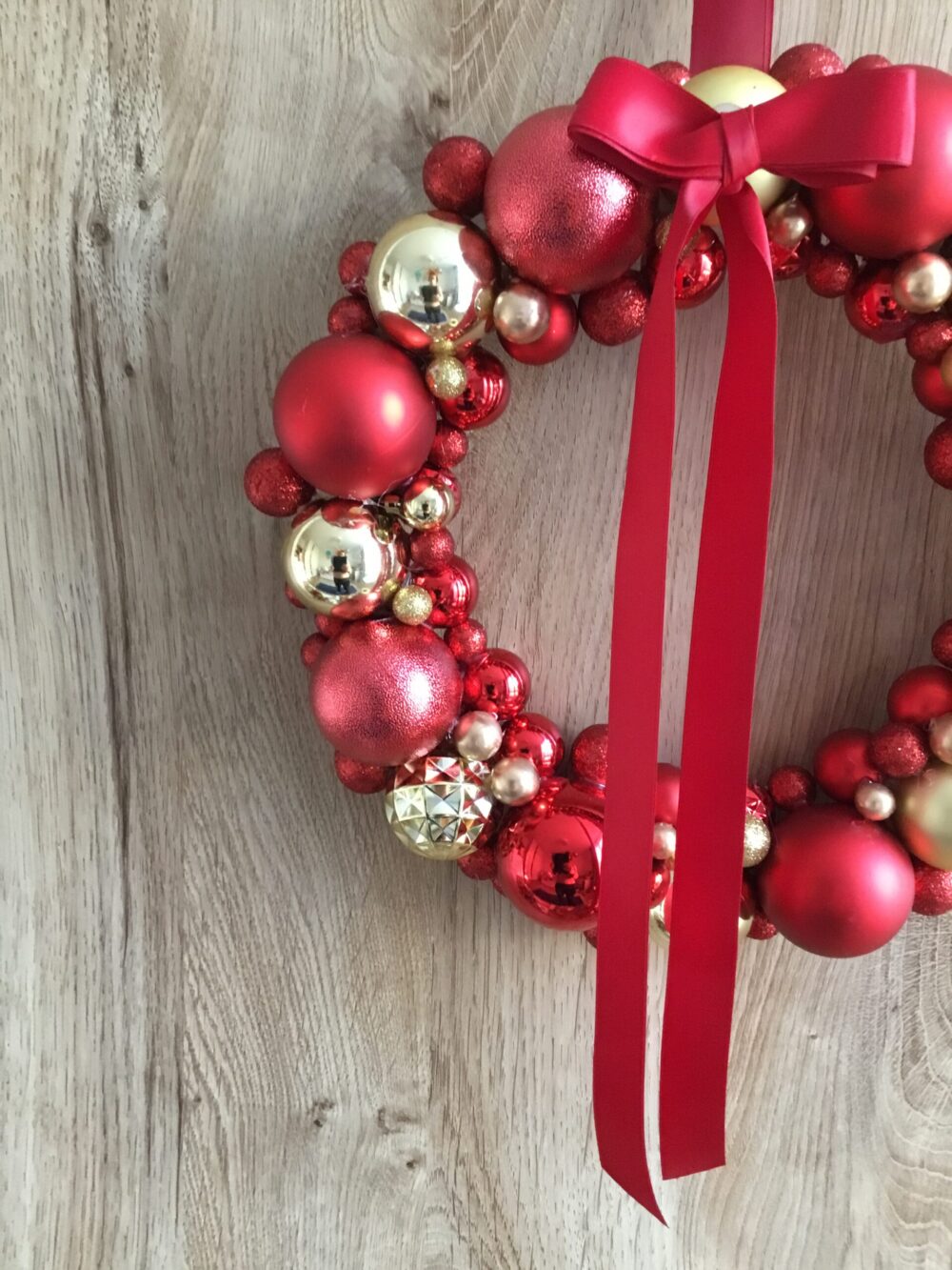 Elegancki wianek świąteczny z czerwonych i złotych ozdób, udekorowany dużą czerwoną wstążką.