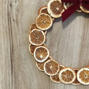 Rustykalny wianek bożonarodzeniowy z suszonymi pomarańczami i bordową aksamitną kokardą na drewnianej podstawie.