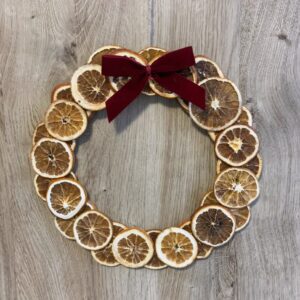 Wianek świąteczny z suszonymi pomarańczami i czerwoną aksamitną wstążką na drewnianej podstawie.
